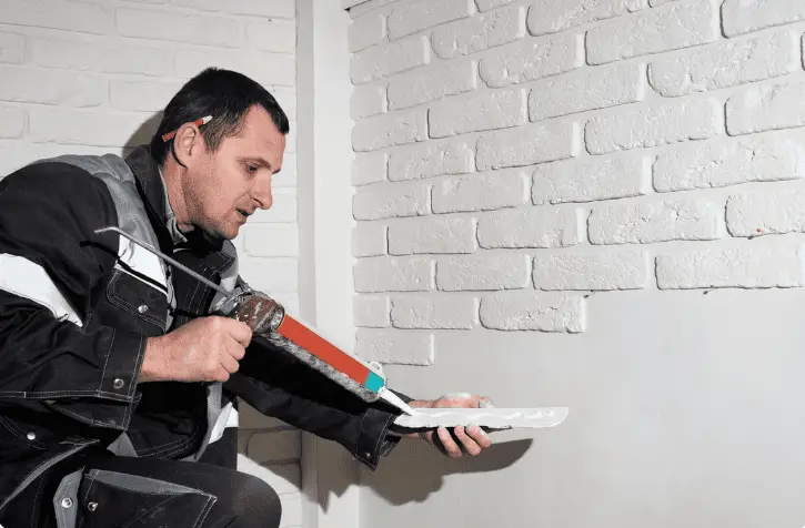 Professional applying cavity wall insulation foam using injection gun on white brick wall