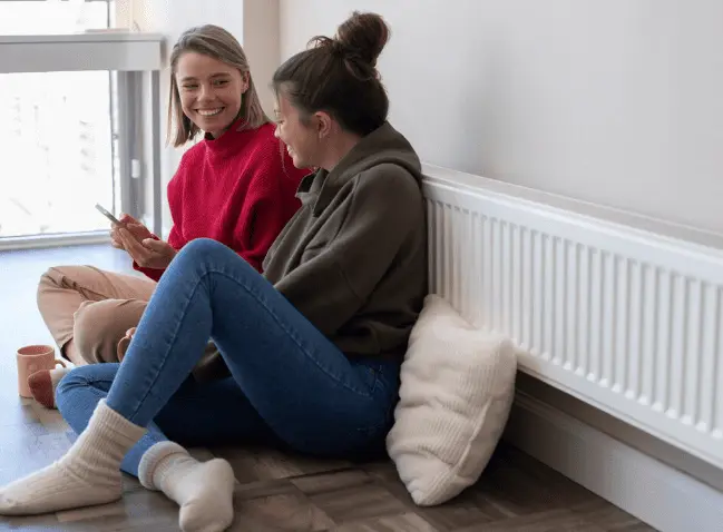 Two women sitting by first time central heating radiator discussing home heating system installation
